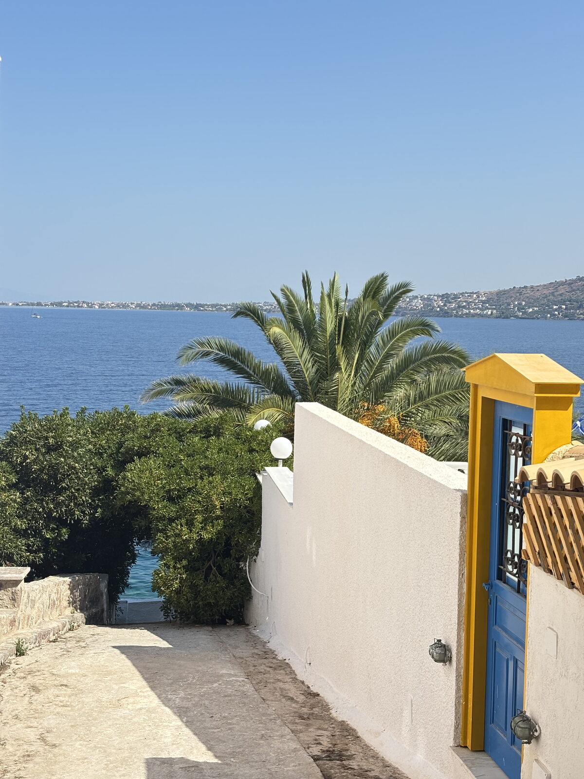 A whitewashed lane in Perdika ending at a blue door and the sea